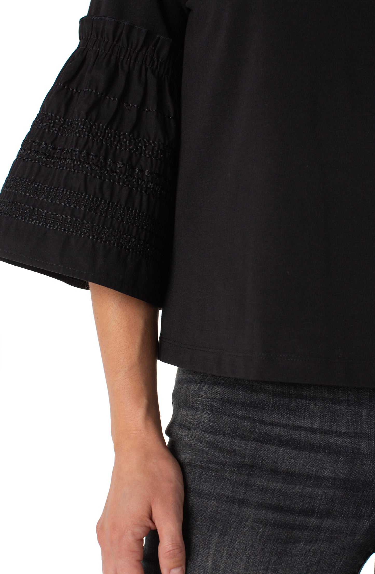 Close-up of a person wearing a black blouse with smocked sleeves on a white background