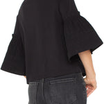 Person wearing a black blouse with ruffled sleeves and gray jeans on a white background