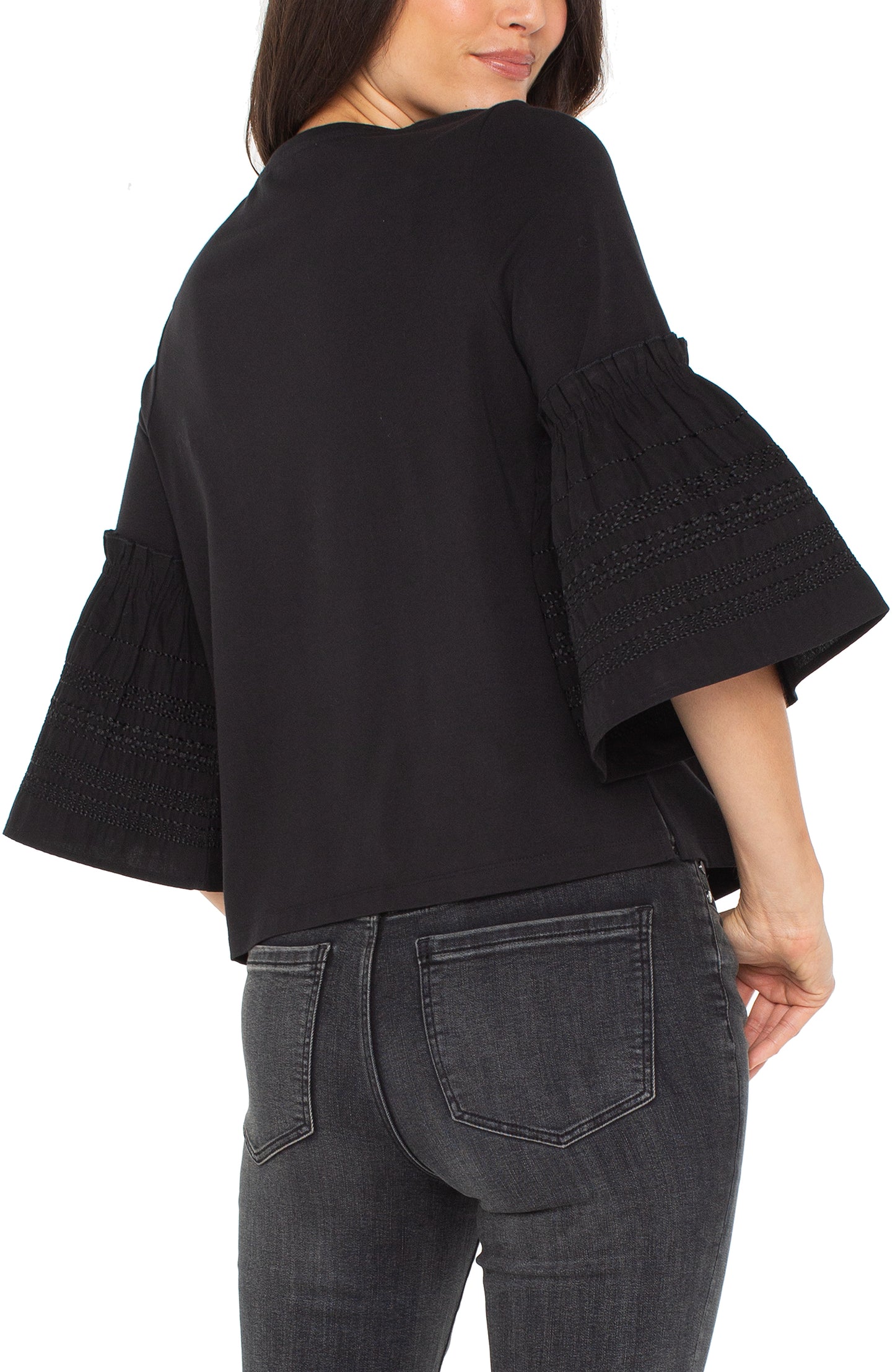 Person wearing a black blouse with ruffled sleeves and gray jeans on a white background