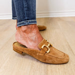 Brown suede loafer worn with rolled-up jeans on a wooden floor.