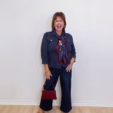 Woman wearing a navy outfit with a red bag and scarf against a white wall.