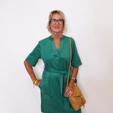 Woman wearing a green dress with a brown bag against a white background