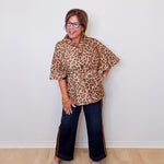 Woman wearing a leopard print top and dark jeans against a white wall.