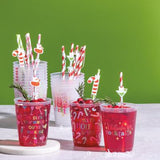 Red cocktails in cups with festive straws on a white surface against a green background