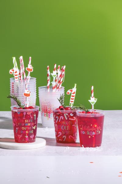 Red cocktails in cups with festive straws on a white surface against a green background