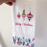 Hand holding a Christmas-themed towel with decorative ornaments and 'Merry Christmas' text.