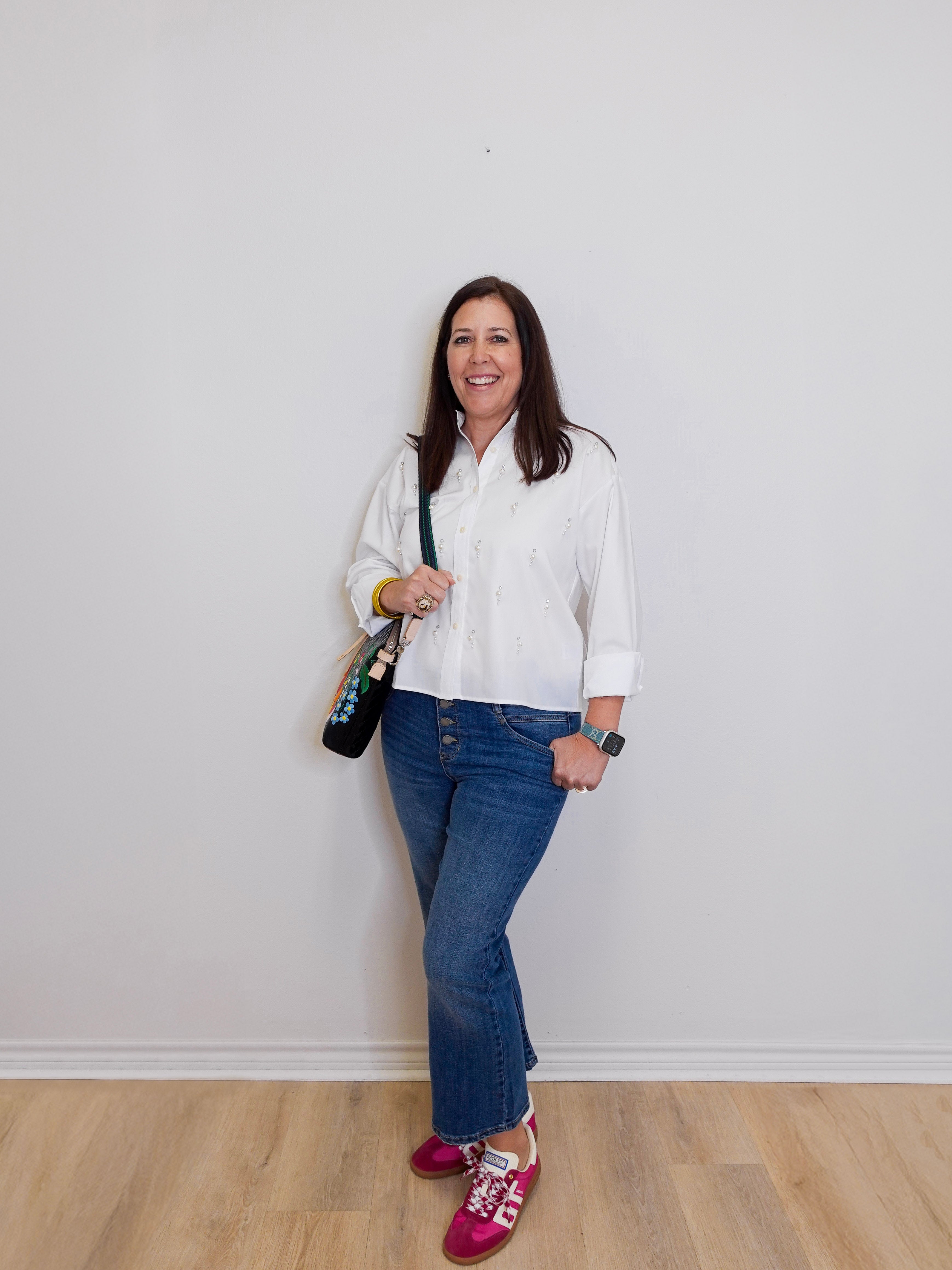 Woman wearing a white shirt, blue jeans, and red shoes against a plain white wall.