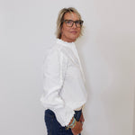 Person wearing a white blouse and blue jeans against a plain background