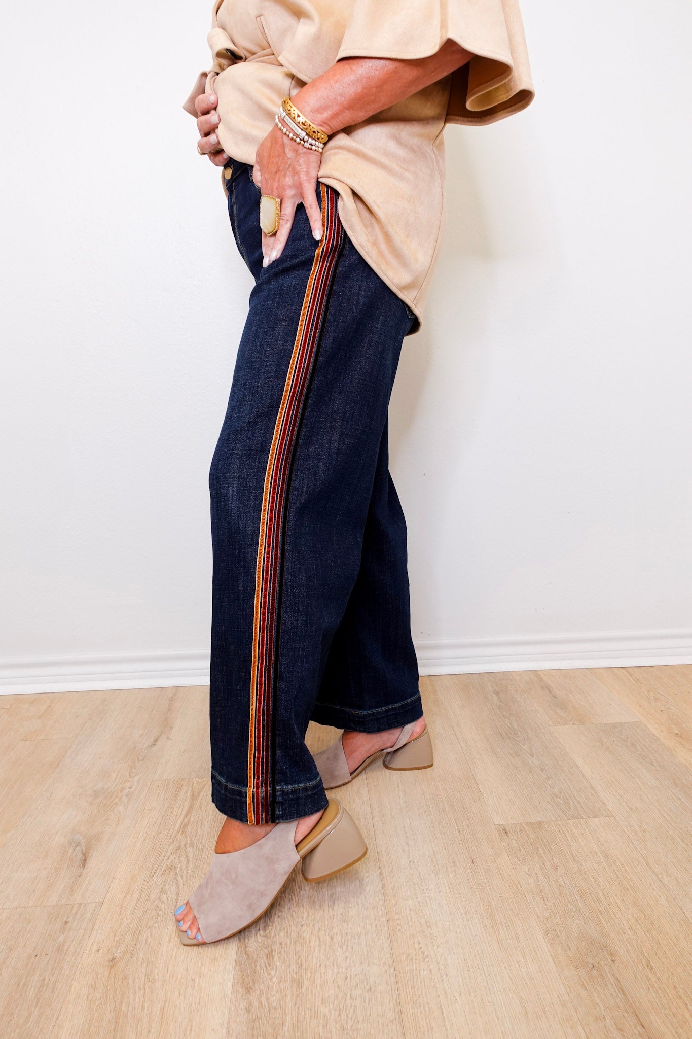 Person wearing dark blue jeans with a striped pattern on a light wooden floor.