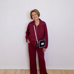 Person wearing a burgundy tracksuit with a black and gold handbag against a white wall.