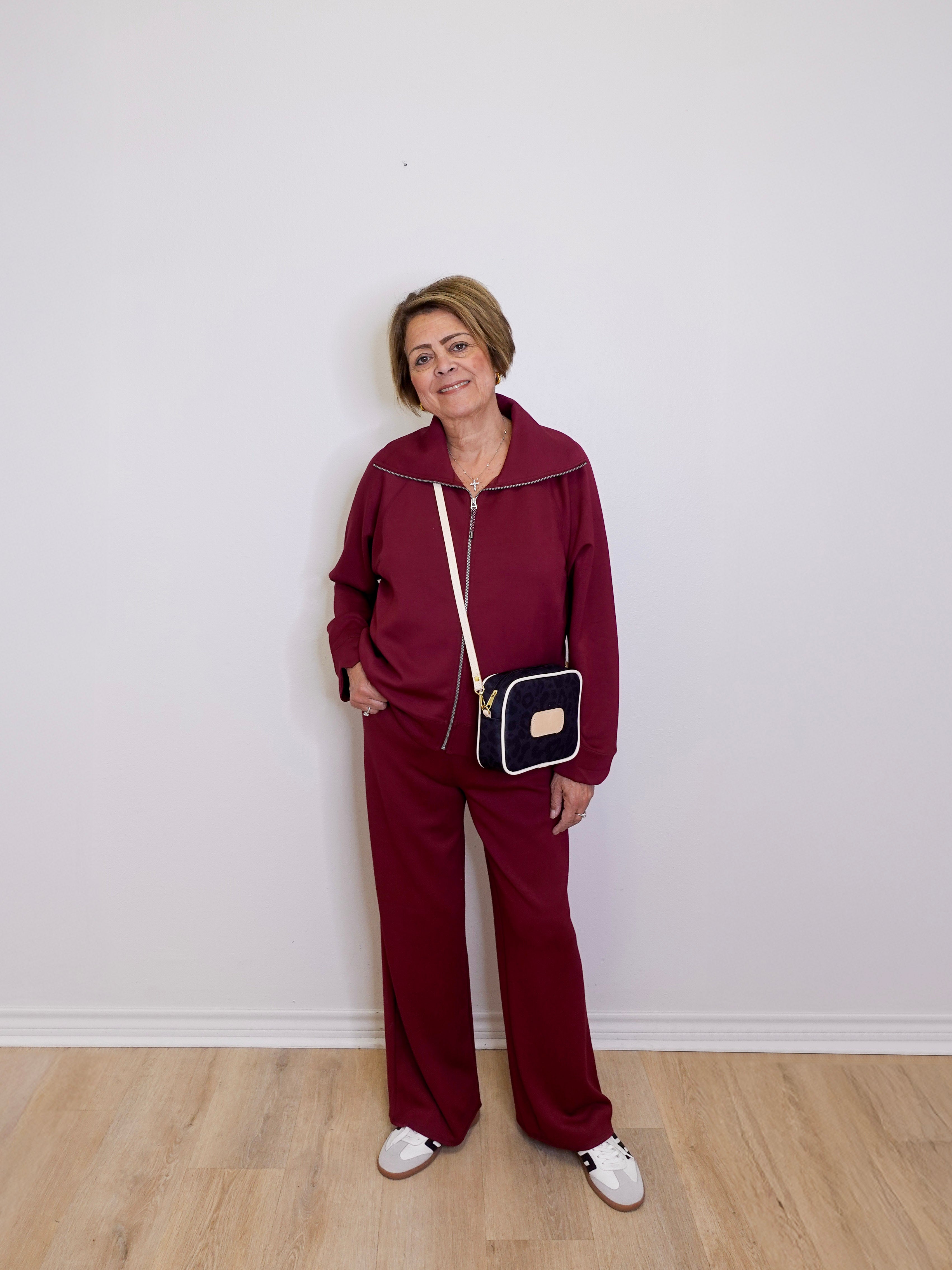 Person wearing a burgundy tracksuit with a black and gold handbag against a white wall.
