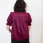 Person wearing a burgundy blouse with puffed sleeves against a white background