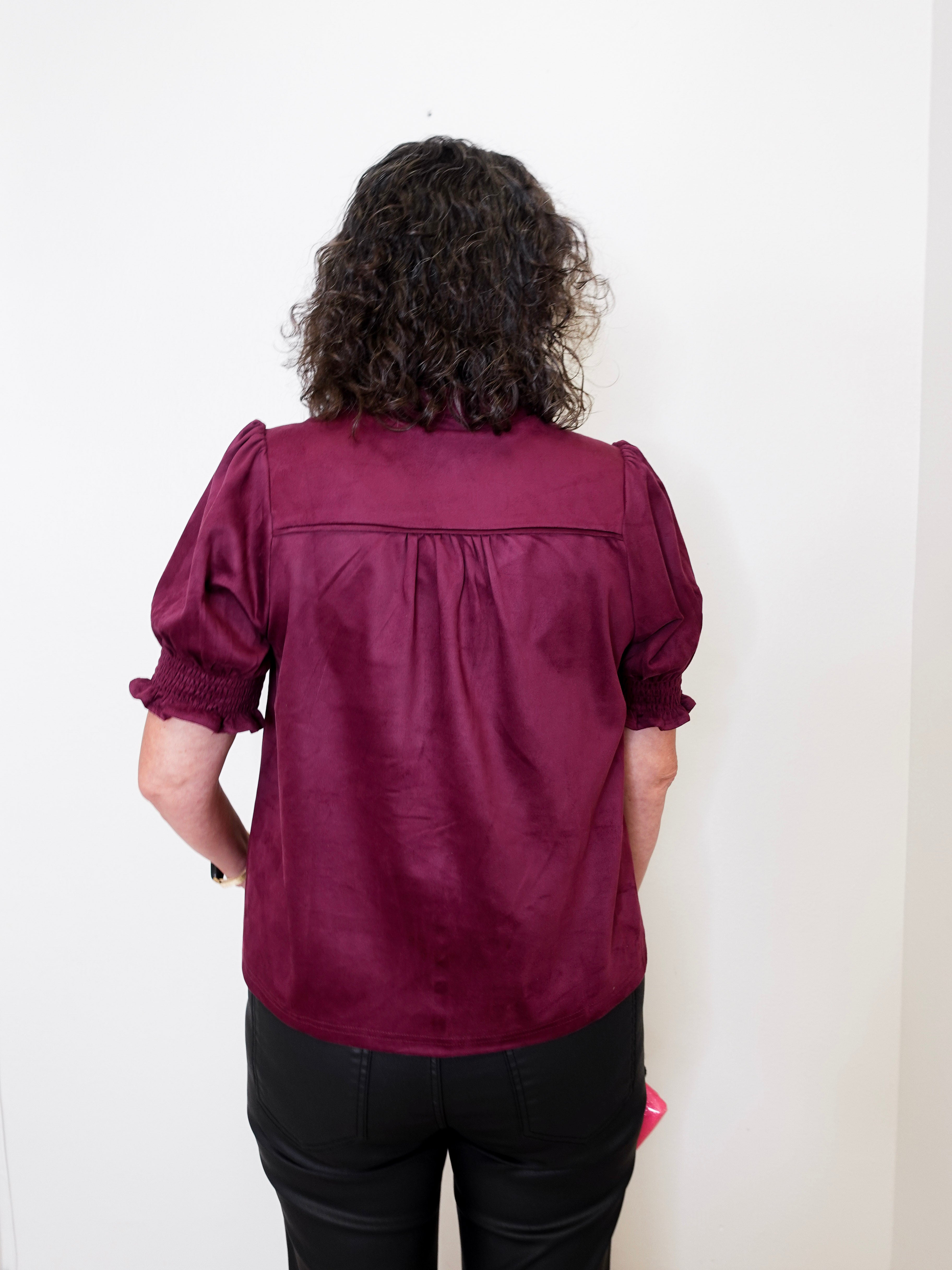 Person wearing a burgundy blouse with puffed sleeves against a white background