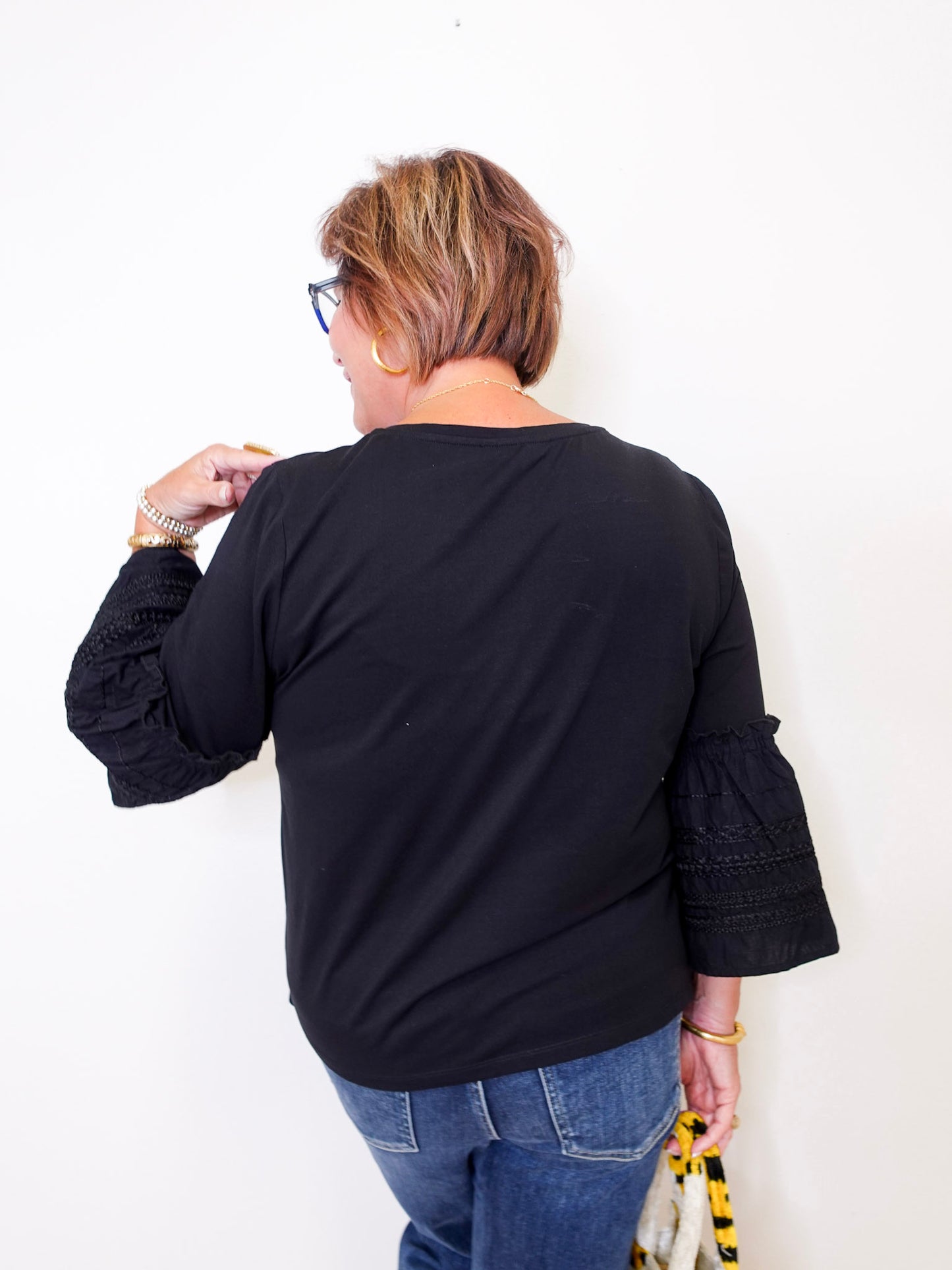 Person wearing a black top with embroidered sleeves against a white background