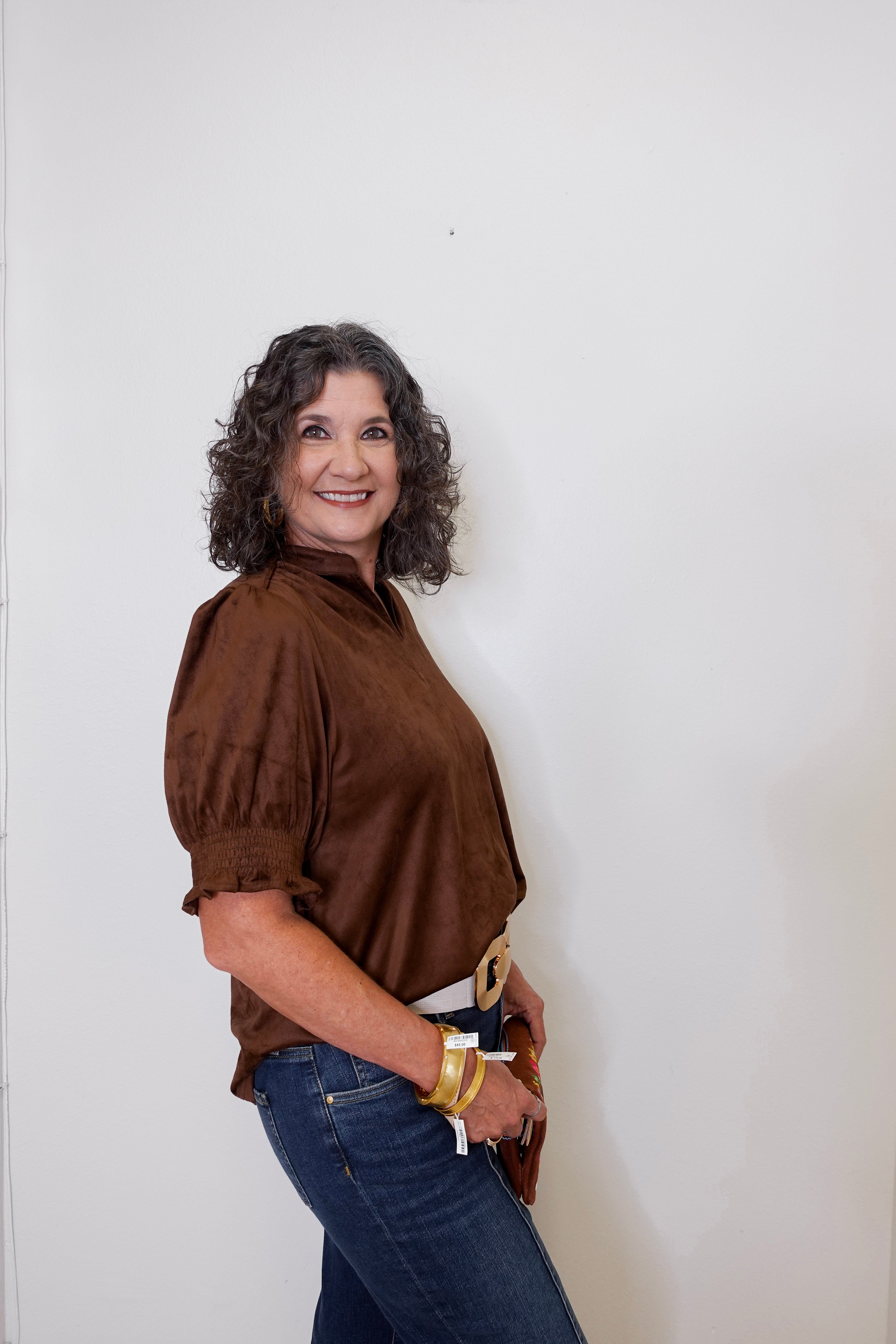 Woman wearing a brown blouse and blue jeans against a white wall