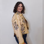 Person wearing a beige embroidered jacket with floral patterns on a plain background