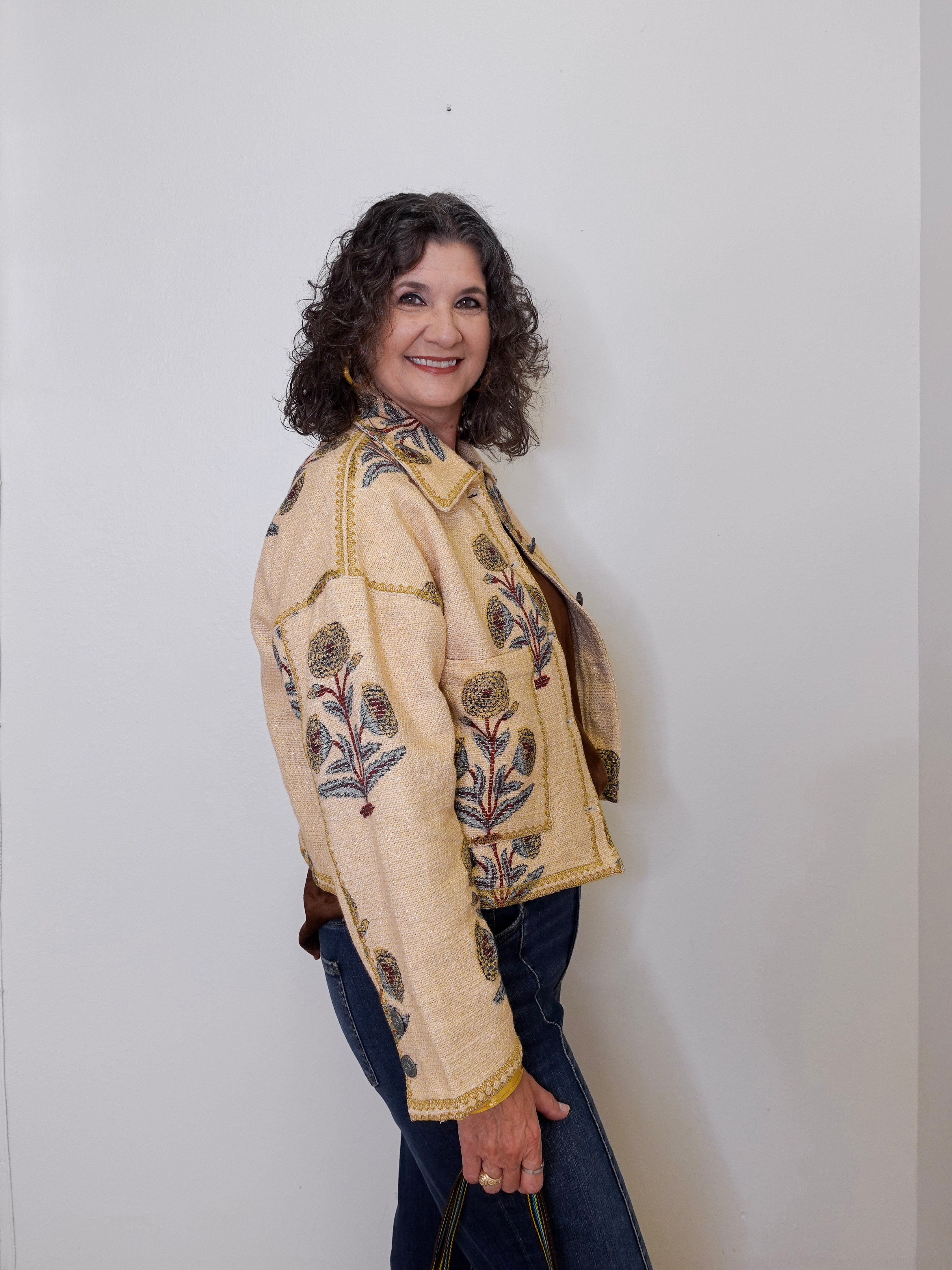 Person wearing a beige embroidered jacket with floral patterns on a plain background