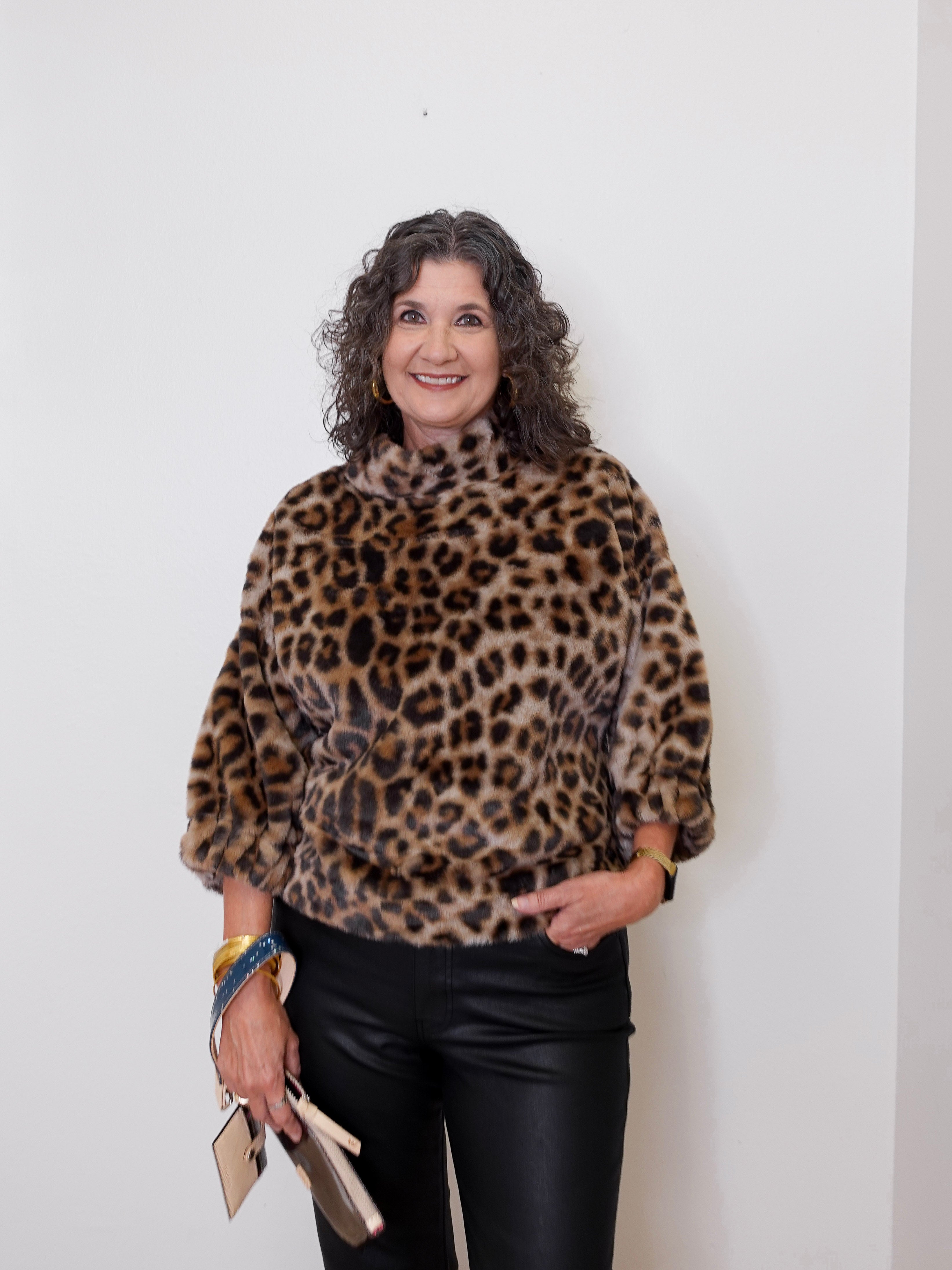 Woman wearing a leopard print sweater against a white wall