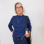 Woman wearing a blue top and jeans, holding a black bag against a white background