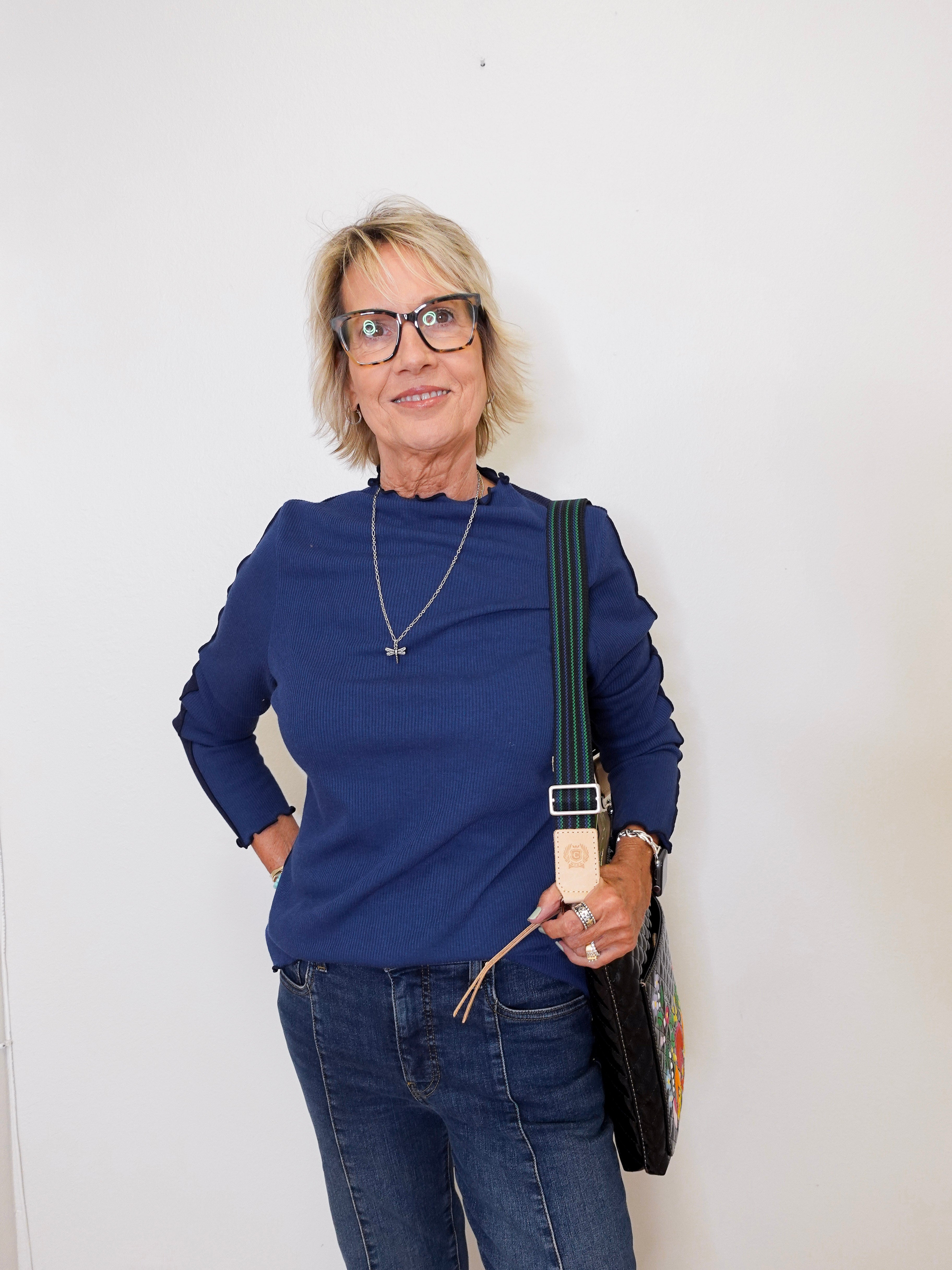 Woman wearing a blue top and jeans, holding a black bag against a white background
