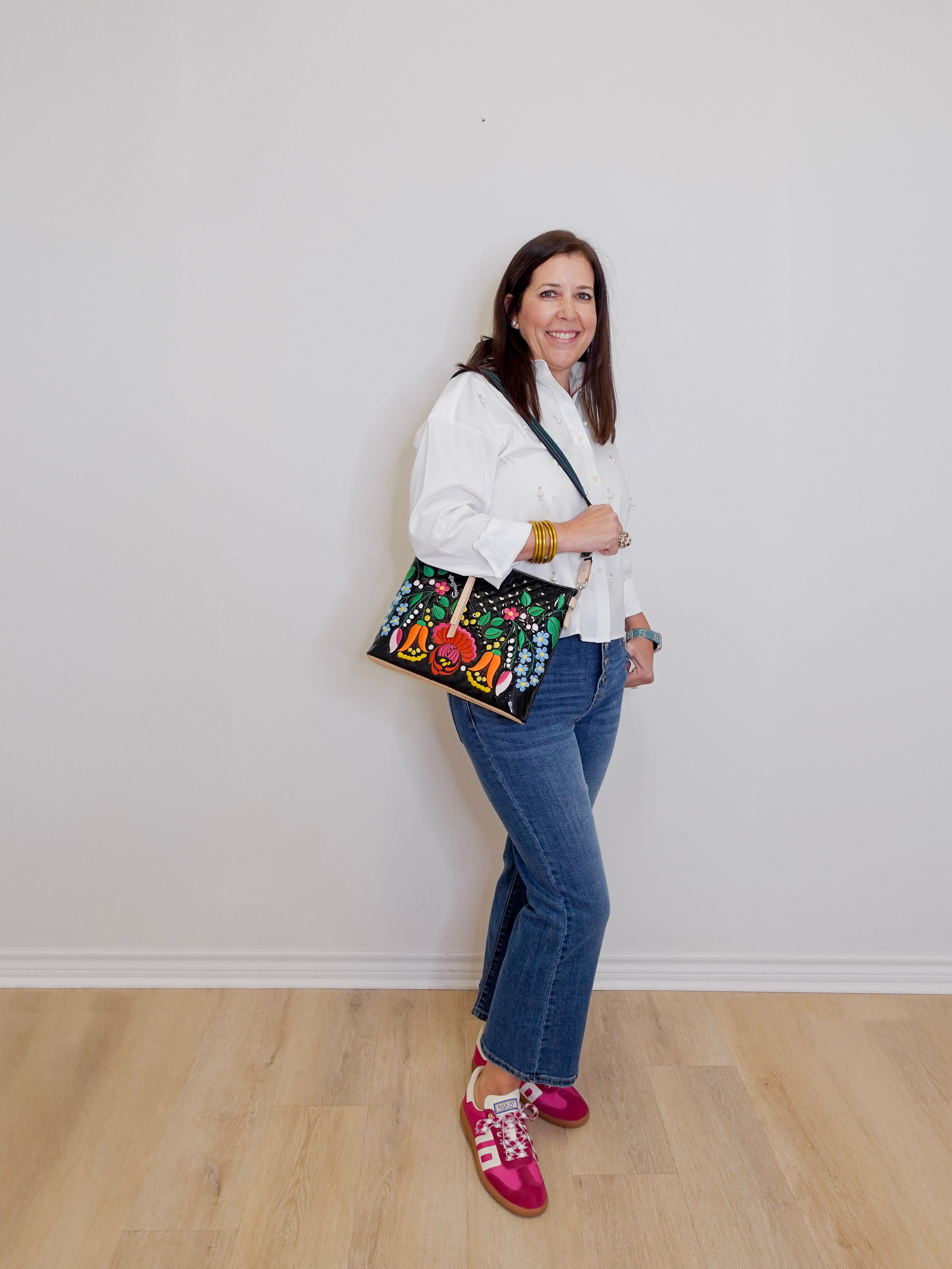 Woman holding a colorful handbag against a white wall