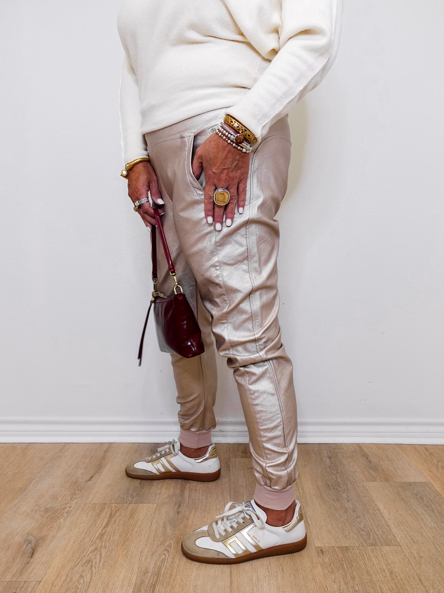 Person wearing beige pants, white sneakers, and multiple bracelets on a light wooden floor.