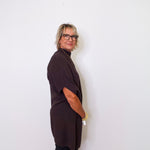 Person wearing a dark brown top and black pants against a white wall.