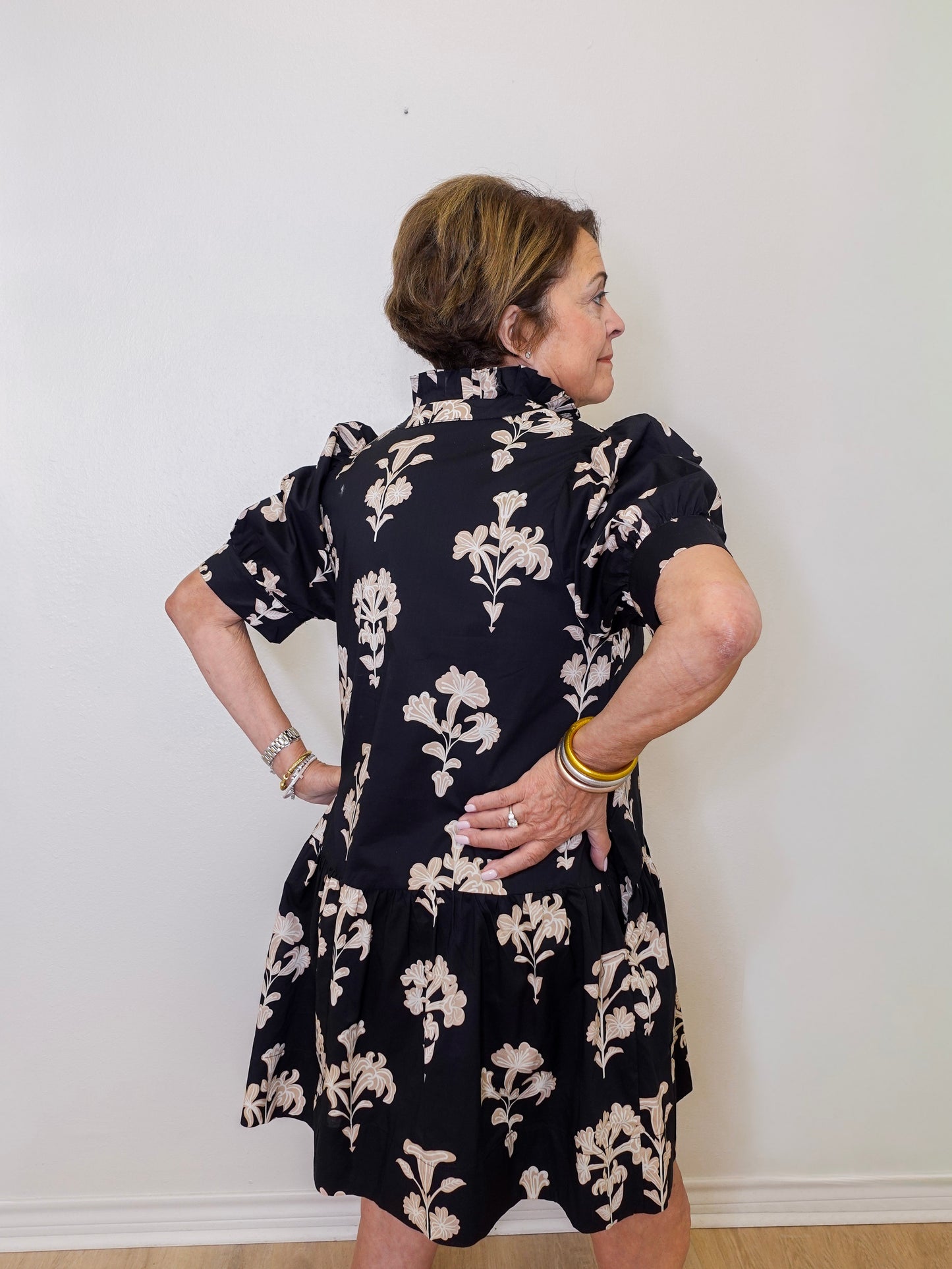 Woman wearing a black floral dress against a white wall
