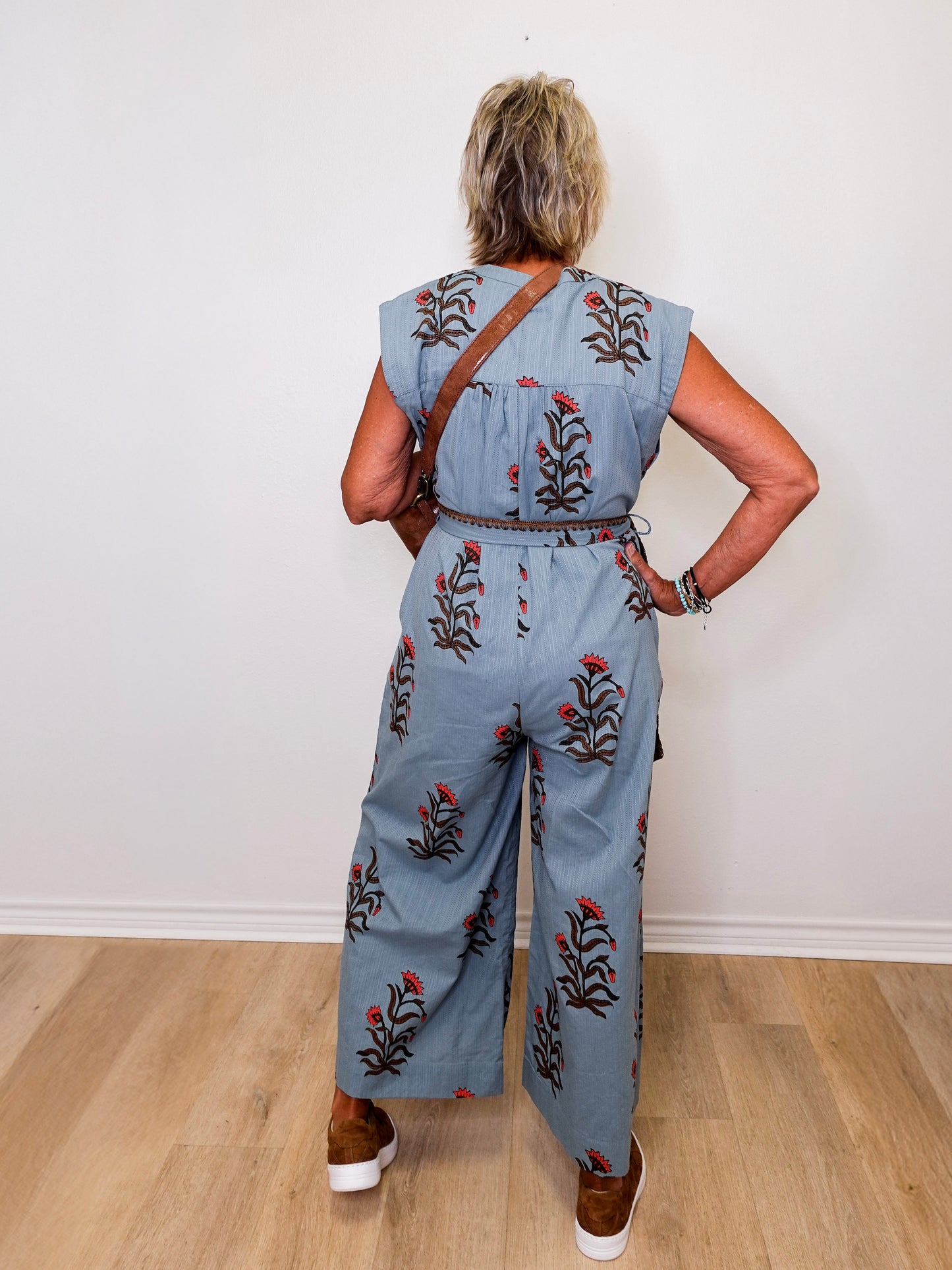 Person wearing a denim jumpsuit with floral embroidery standing against a white wall.