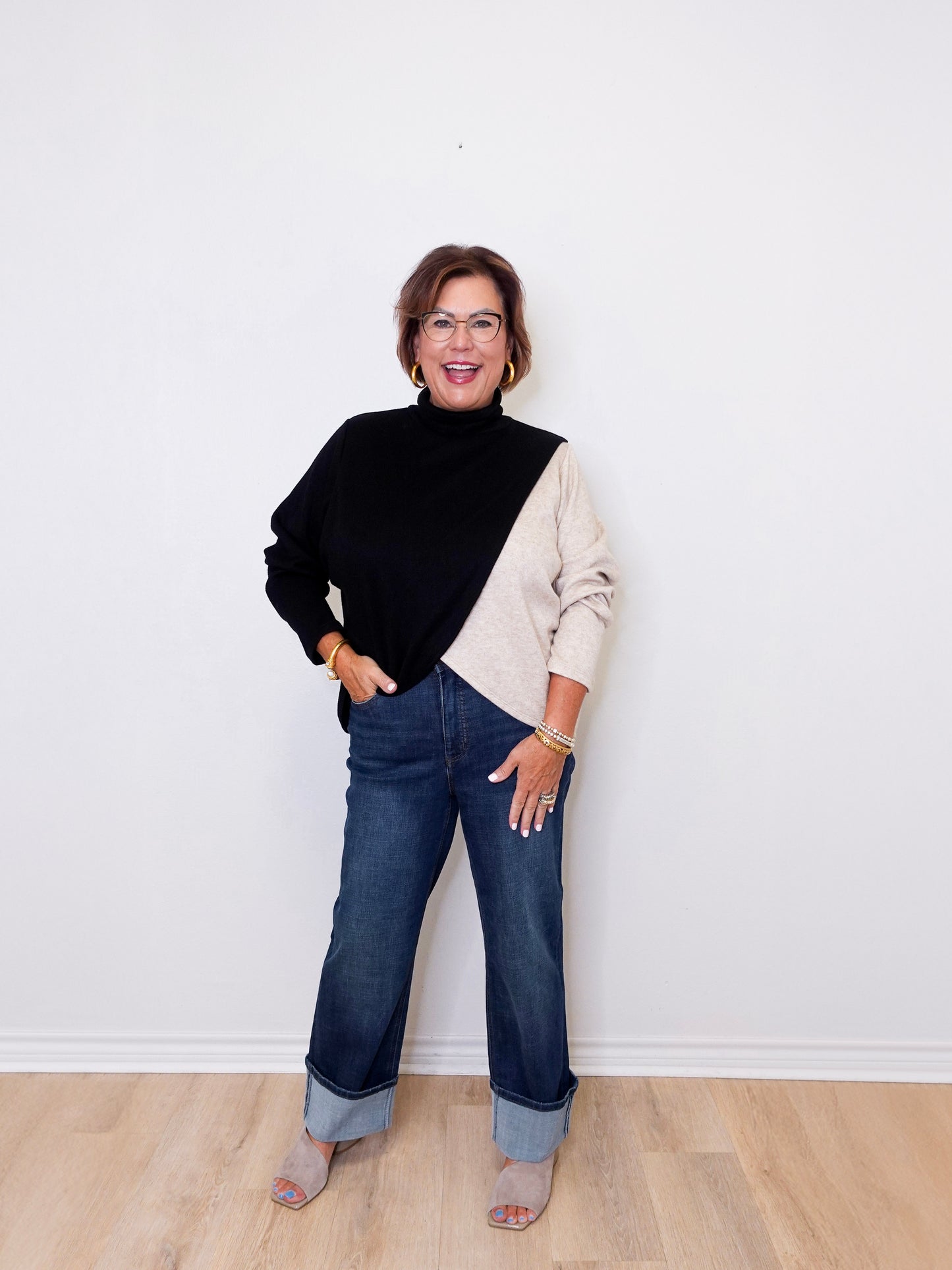 Woman wearing a black and beige sweater with blue jeans against a white wall.