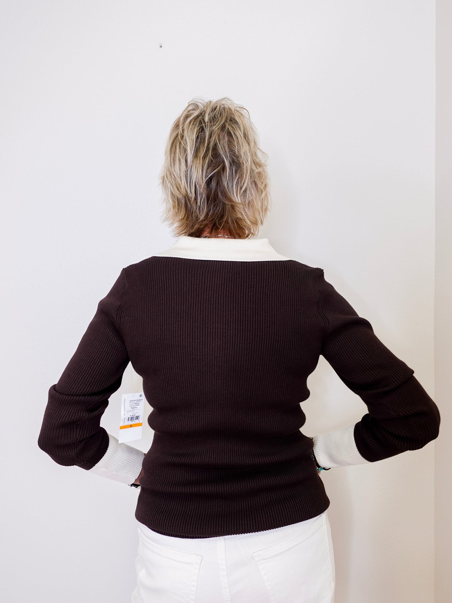 Person wearing a black sweater with a white collar against a plain background