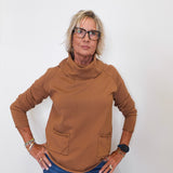 Stylish fall look: woman wearing a tan cowl neck sweater with denim jeans against white backdrop.