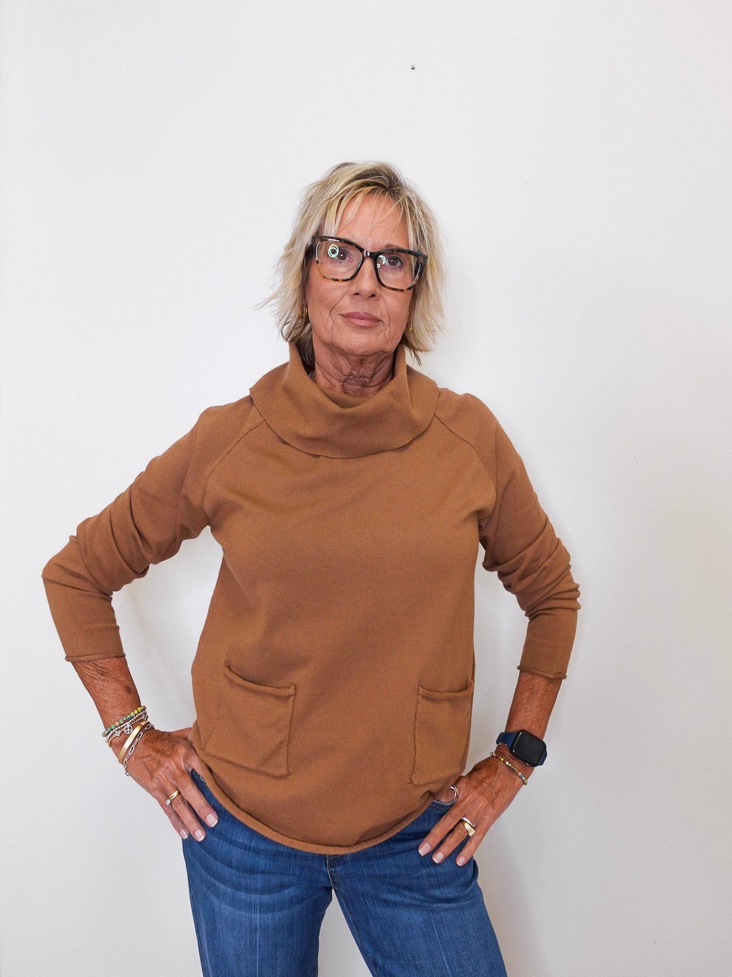 Stylish fall look: woman wearing a tan cowl neck sweater with denim jeans against white backdrop.