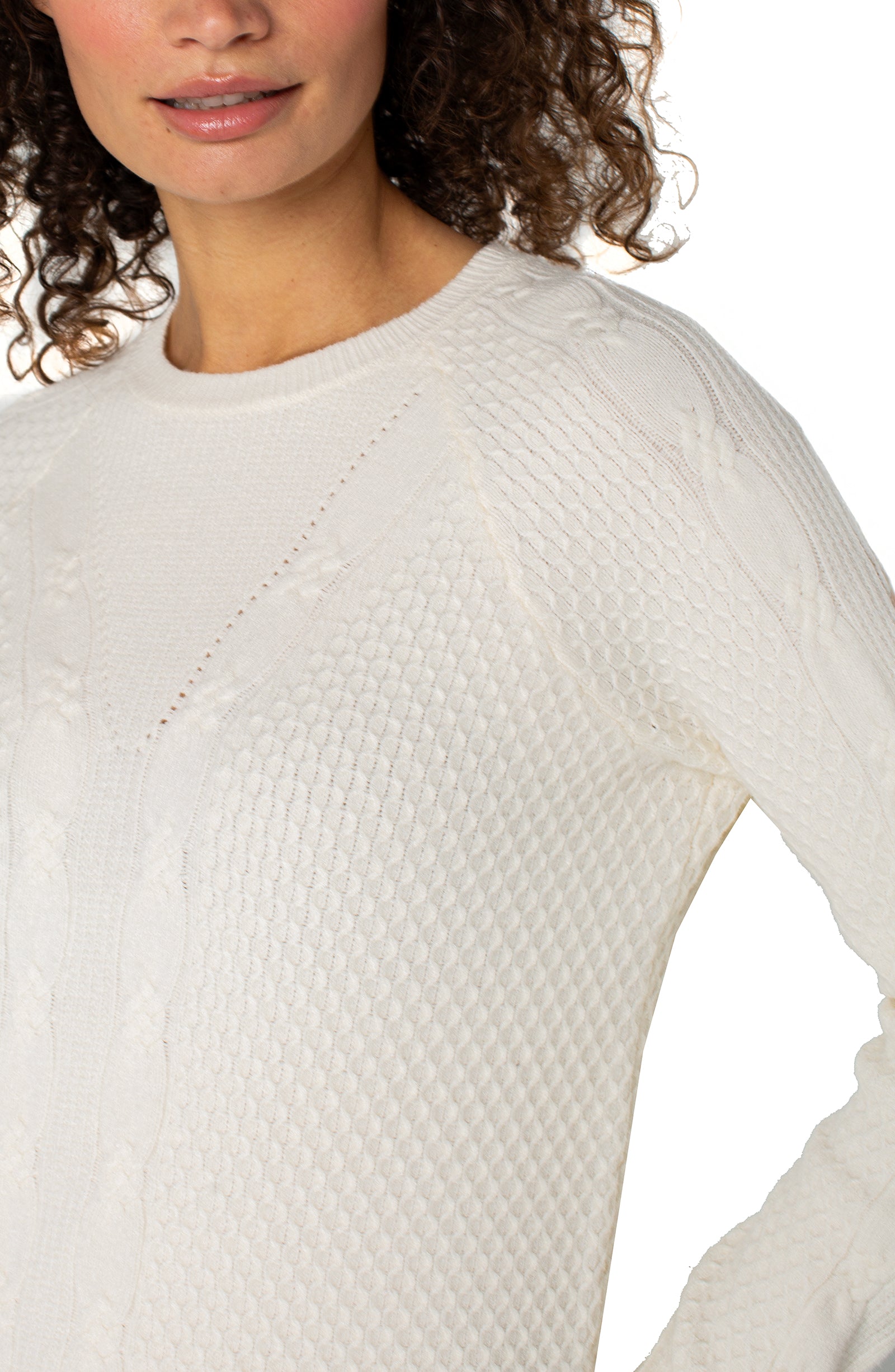 Close-up of a person wearing a textured white sweater on a plain background
