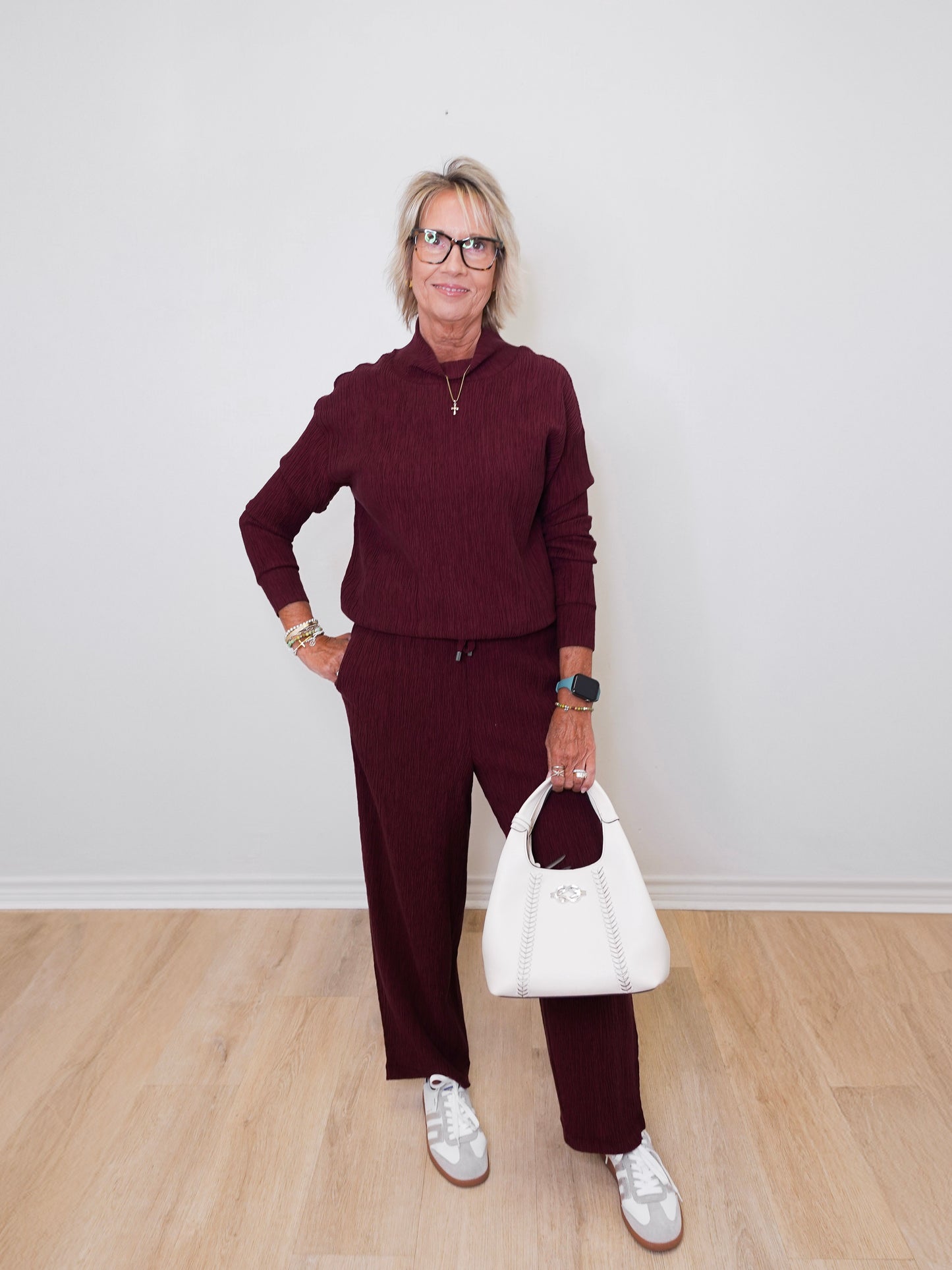 Woman wearing a burgundy outfit with a white handbag against a plain background