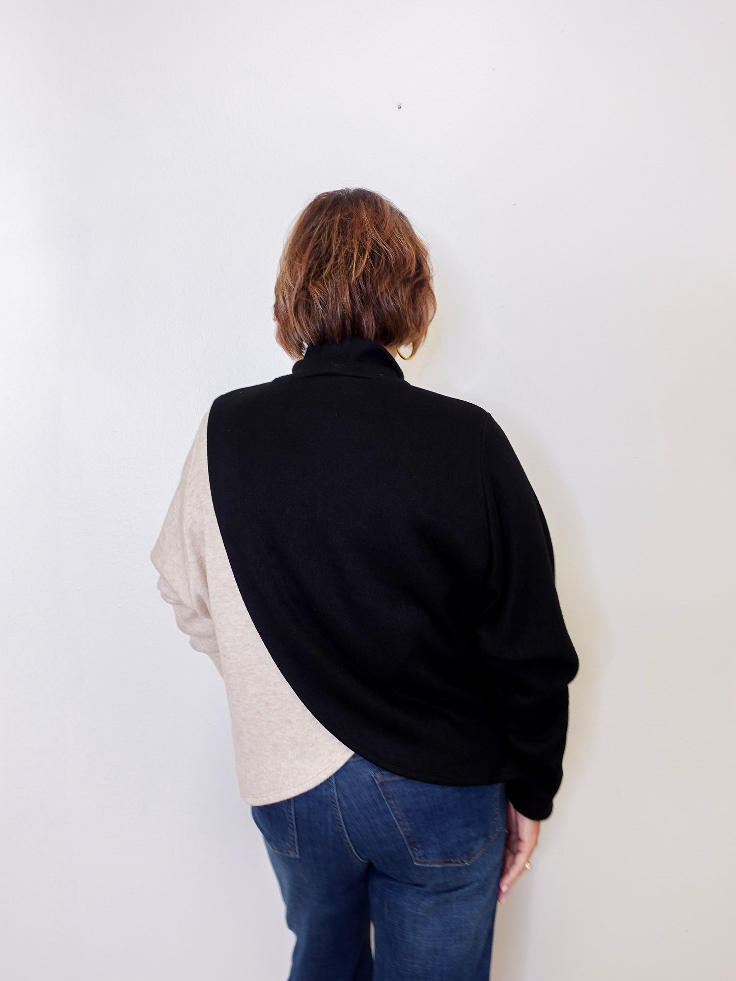 Person wearing a black and beige shirt with blue jeans on a white background