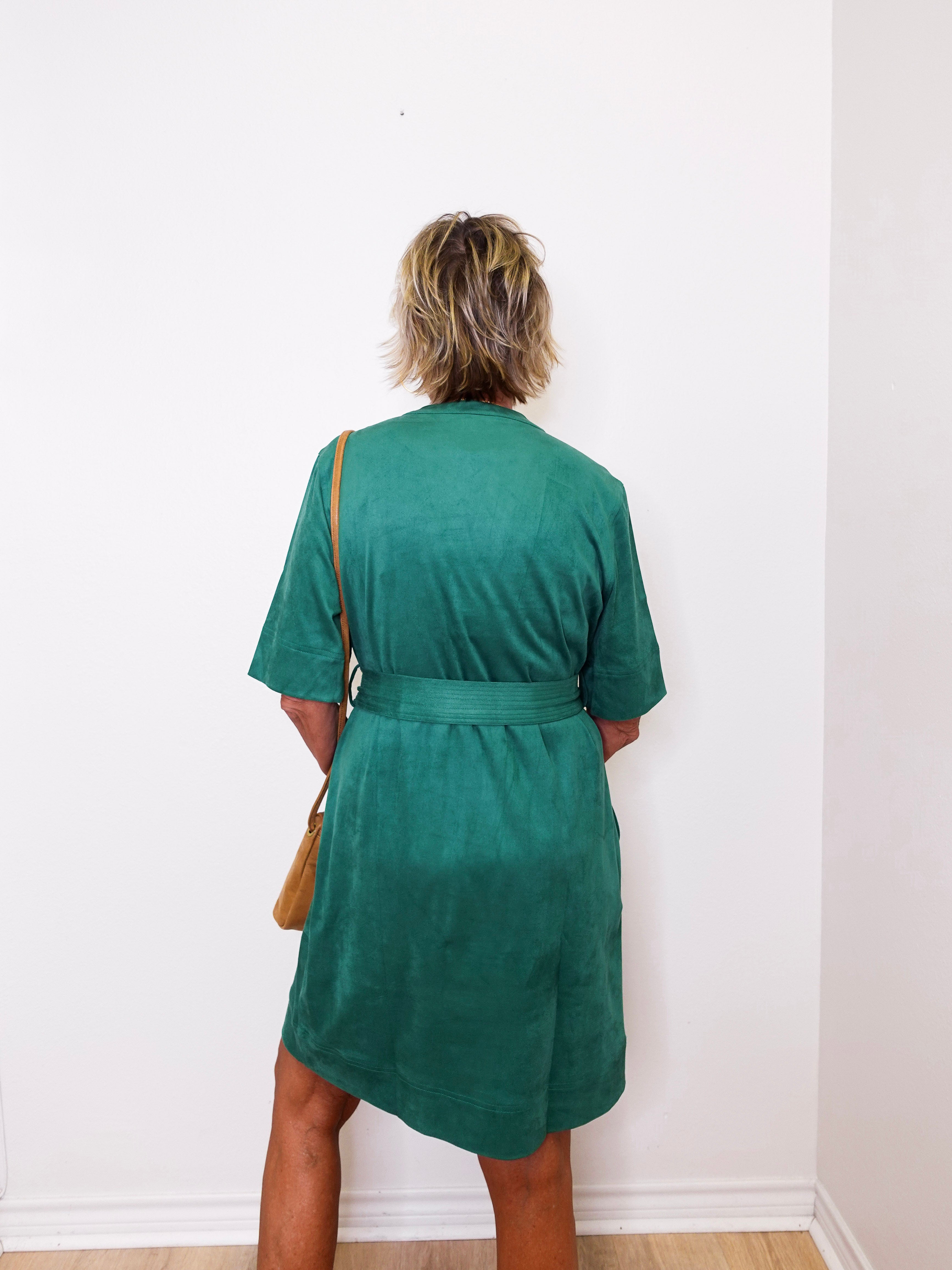 Person wearing a green dress against a white wall
