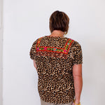 Person wearing a leopard print top with colorful embroidery against a white wall