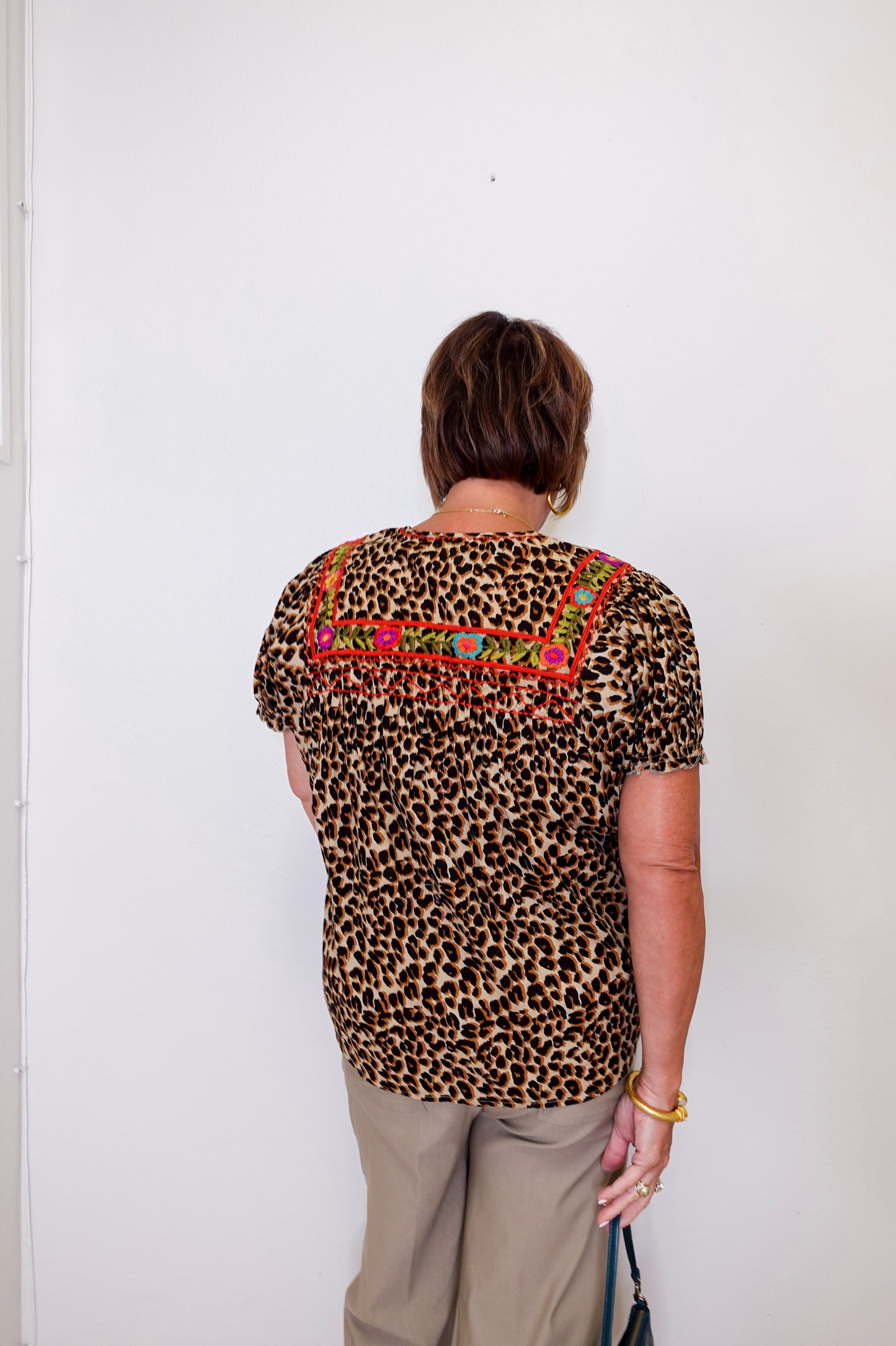 Person wearing a leopard print top with colorful embroidery against a white wall