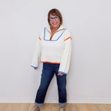 Person wearing a colorful sweater and jeans standing against a white wall.