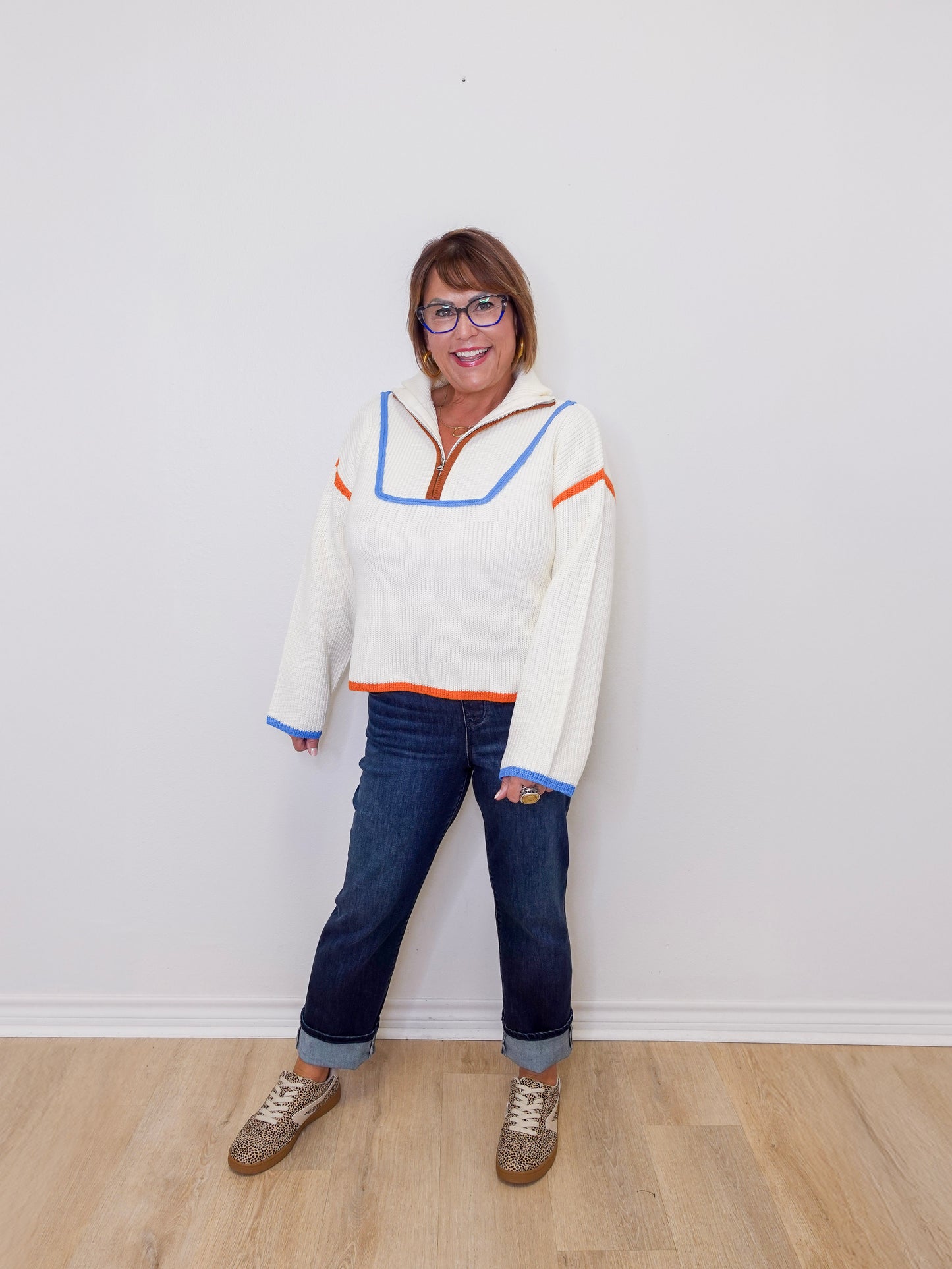 Person wearing a colorful sweater and jeans standing against a white wall.
