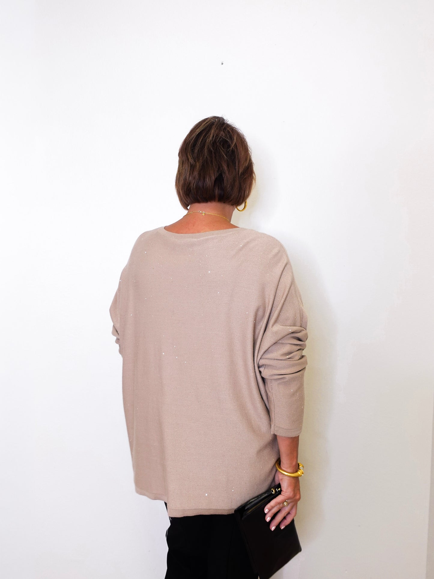 A woman wearing a v-neck jewel embellished sweater in front of a white wall.