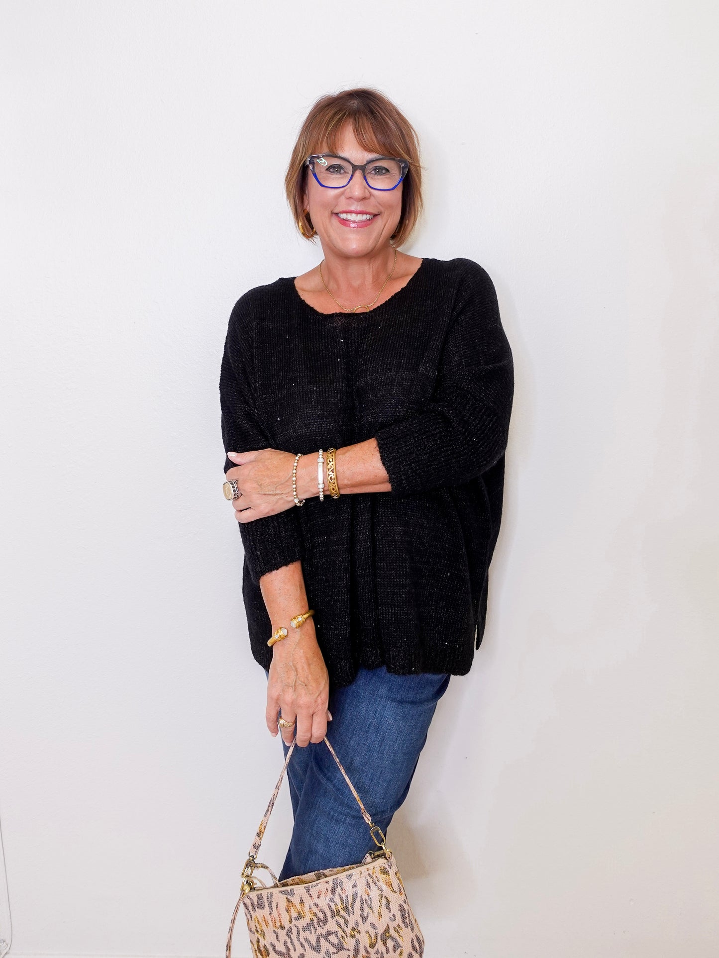 Woman wearing a black sweater and blue jeans, holding a patterned handbag against a white background