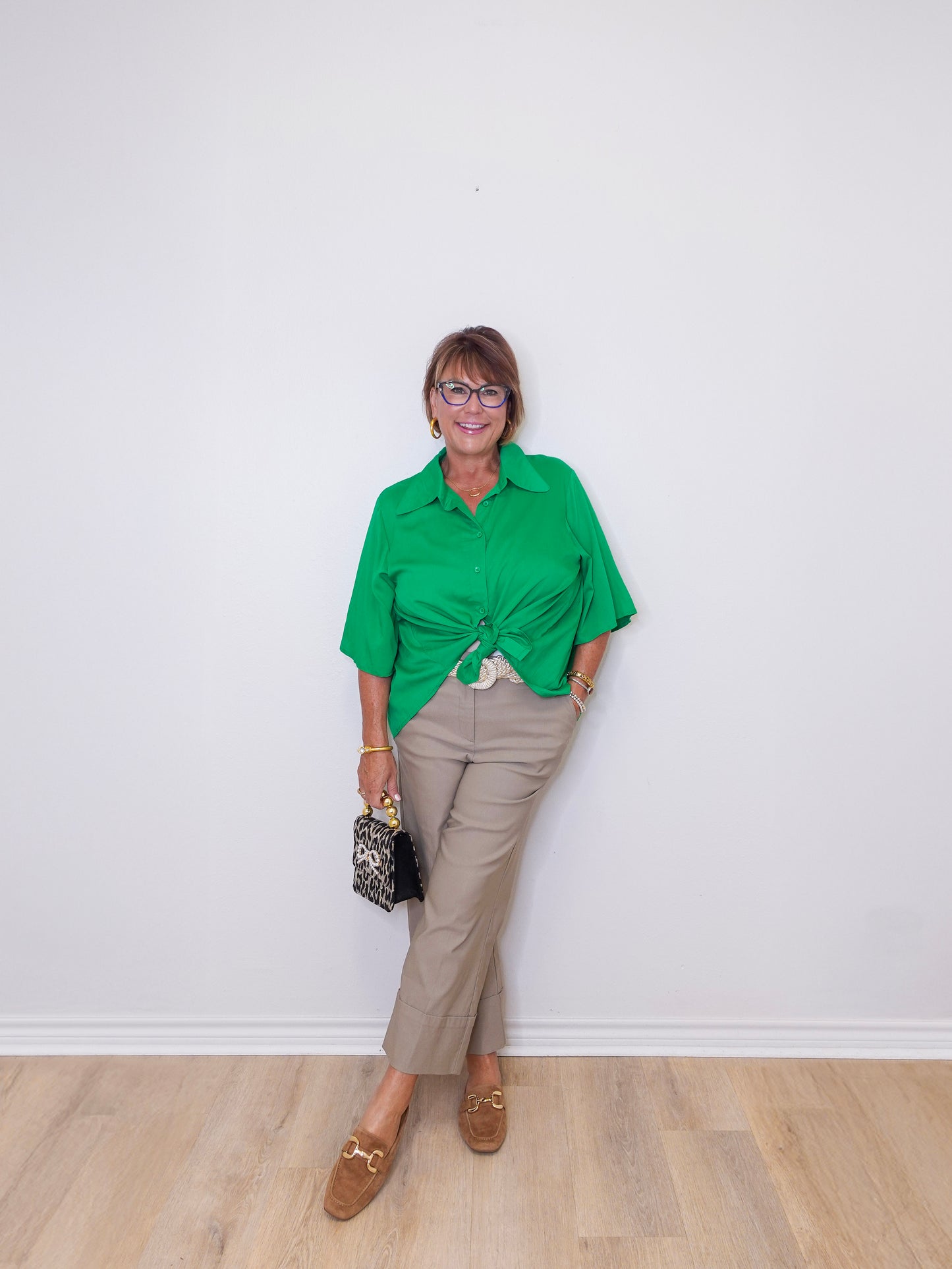 Woman wearing a green shirt and beige pants against a white wall.