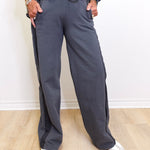 Person wearing gray sweatpants on a light wooden floor with a white wall background