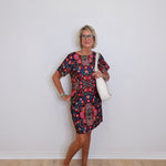 Woman wearing a patterned dress with a white bag against a plain background