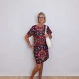 Woman wearing a patterned dress with a white bag against a plain background