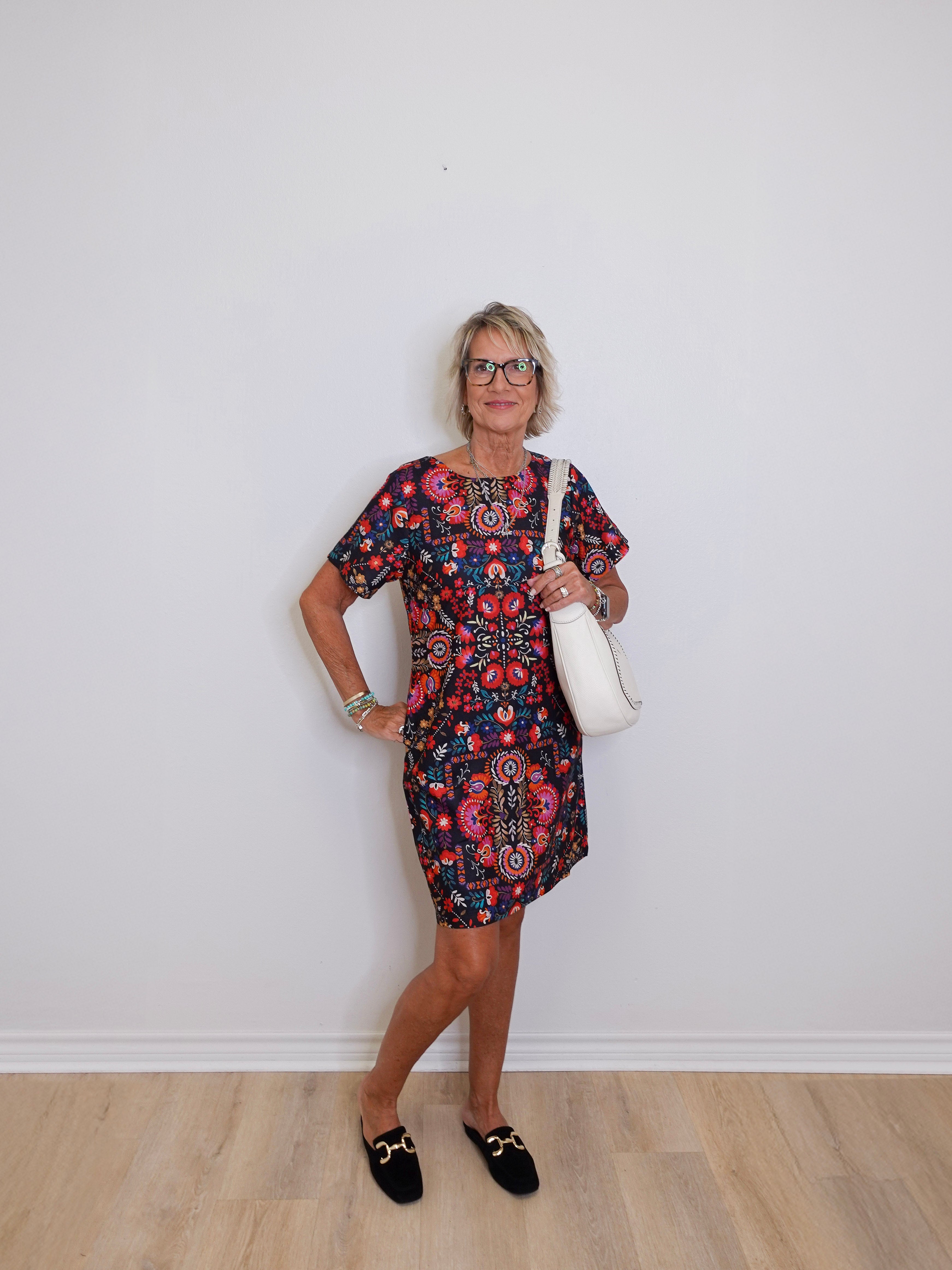 Woman wearing a patterned dress with a white bag against a plain background