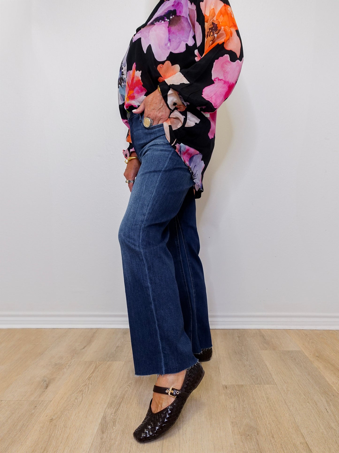 Person wearing a floral top and blue jeans standing against a white wall.