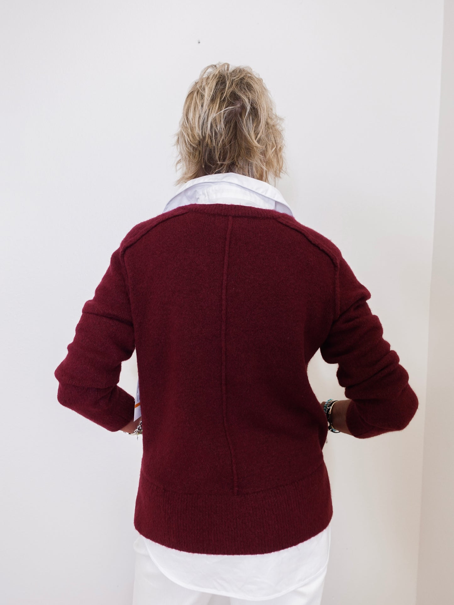 Person wearing a burgundy jacket with a white shirt underneath against a plain background